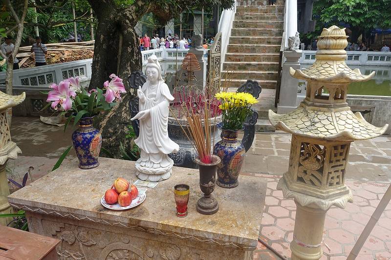Ban thờ ngoài trời có tượng Quan Âm trắng, bát hương và hai đèn đá, phía sau là cầu thang