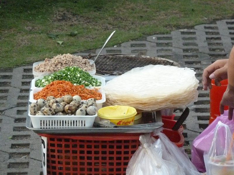 Xe bánh tráng nướng với khay trứng cút, tôm khô, hành lá và chồng bánh tráng