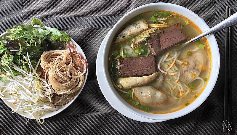 Tô bún bò Huế cạnh đĩa rau sống, giá và bắp chuối bào
