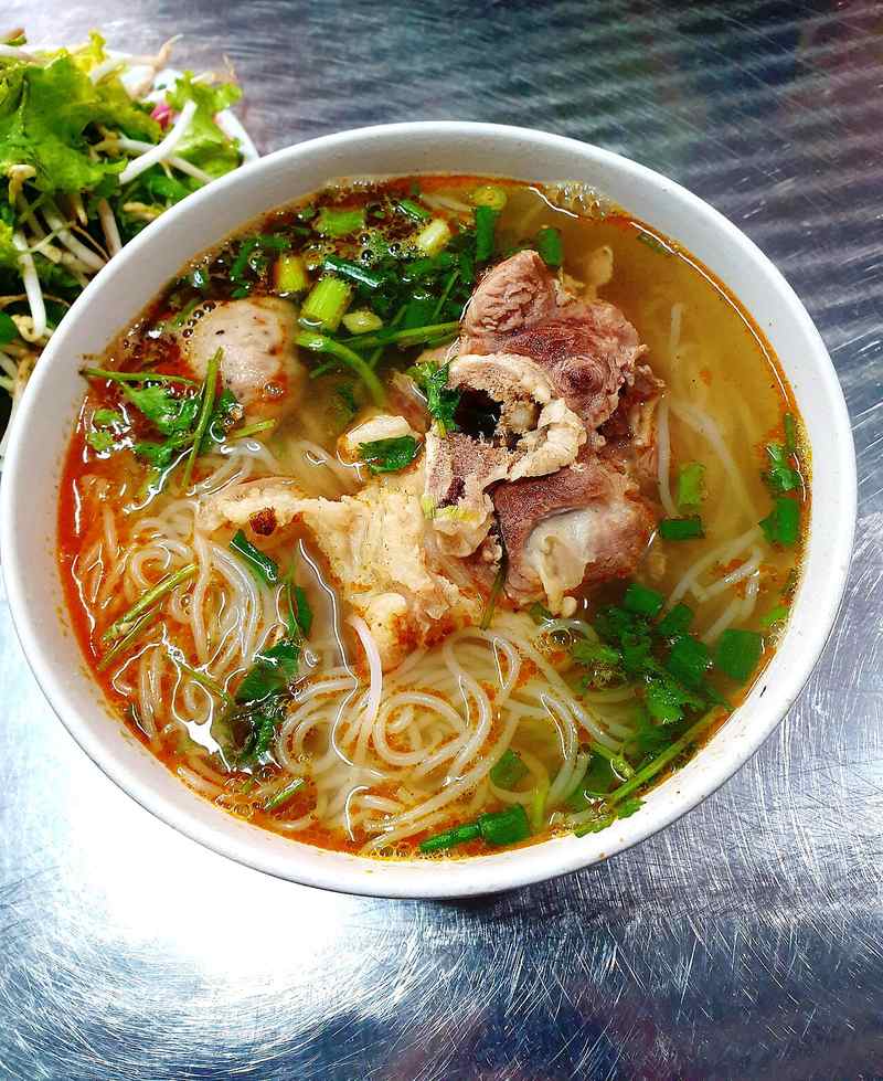 Tô bún bò có giò heo, chả và rau thơm, bên cạnh đĩa rau