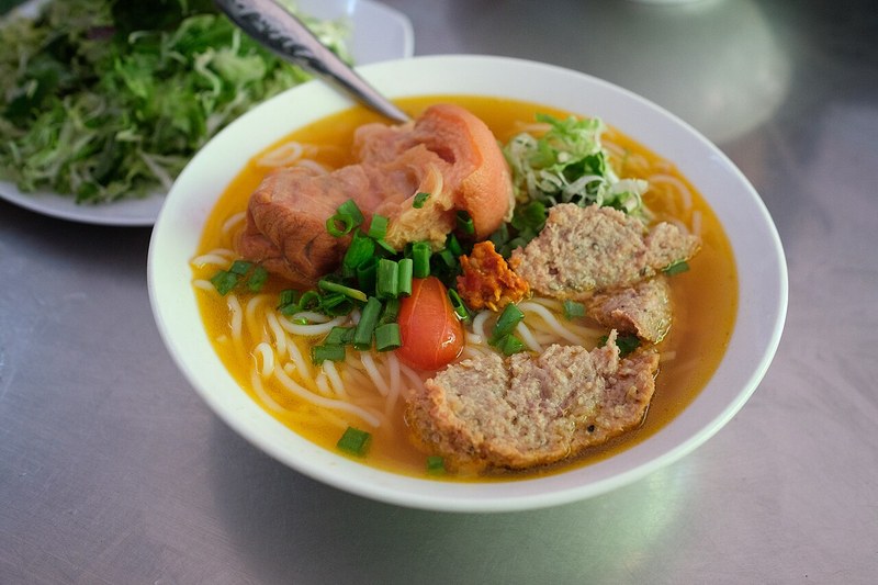 Tô bún bò với giò heo, chả cua và cà chua bên đĩa rau sống
