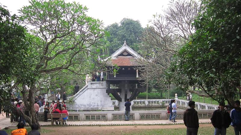 Chùa Một Cột nhìn từ xa giữa hàng cây, khách đi bộ trên sân