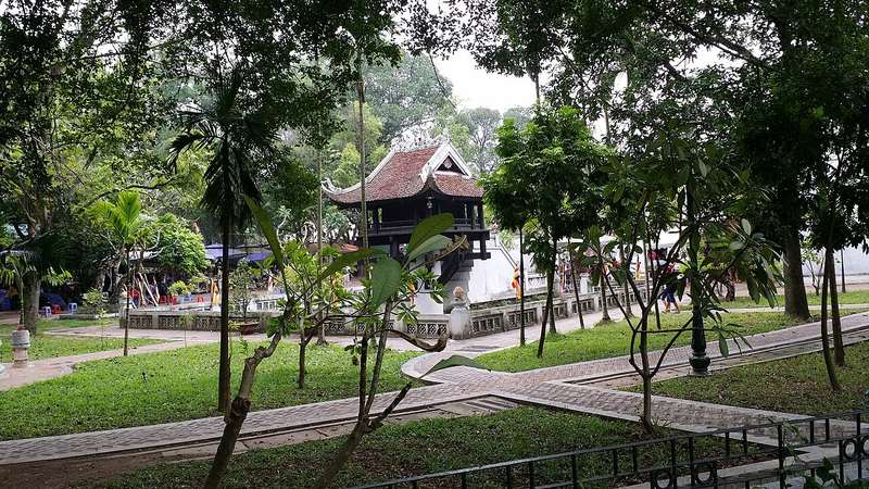 Bãi cỏ và hàng cây trong công viên, phía xa là chùa Một Cột