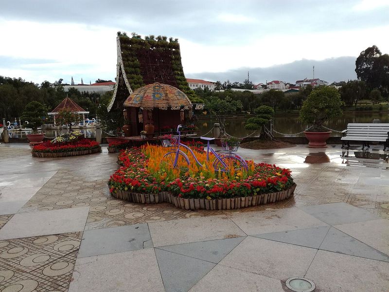 Khu trung tâm vườn hoa với bồn hoa và mô hình nhà mái tranh