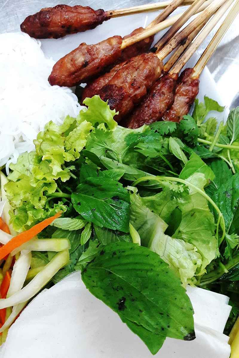 Nem lụi xiên que bên đĩa rau xanh và bánh tráng